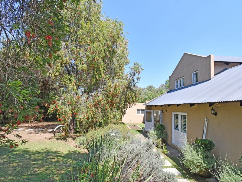 Rear view of the property featuring a pitched corrugated metal roof, plastered exterior walls, and access via french doors to the garden area.