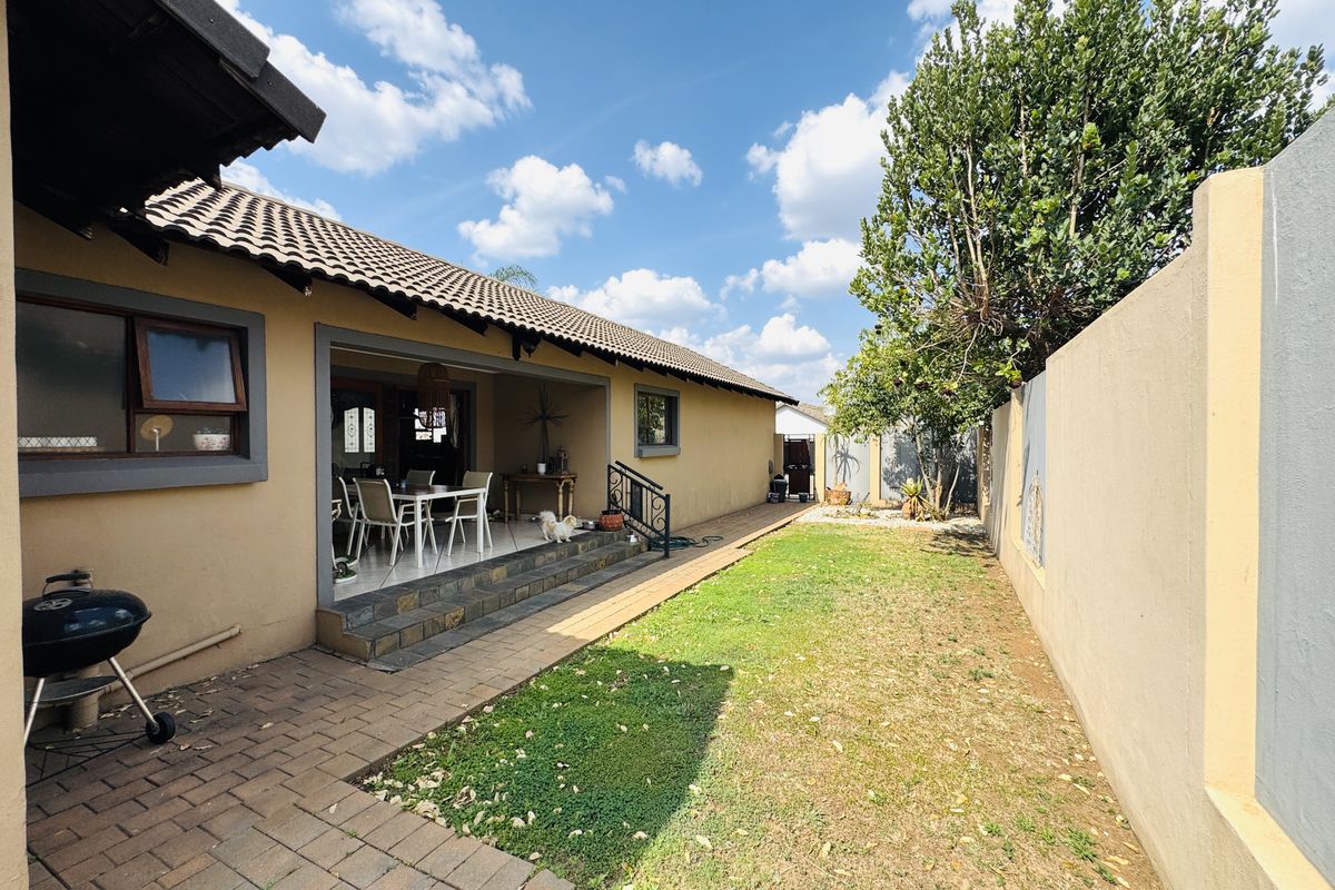 Rear view of the property featuring a paved patio area, a small lawn, and a high boundary wall for privacy.