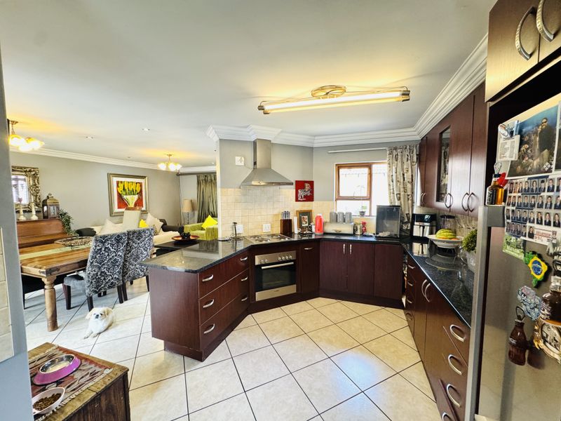 Open-plan kitchen and dining area featuring dark wood cabinetry, granite countertops, stainless steel appliances, and tiled flooring throughout.