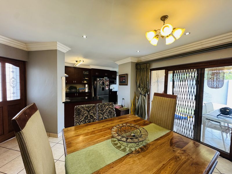 Open-plan dining and kitchen area featuring dark wood cabinetry, granite countertops, crown molding, and sliding glass doors leading to the outdoor patio.