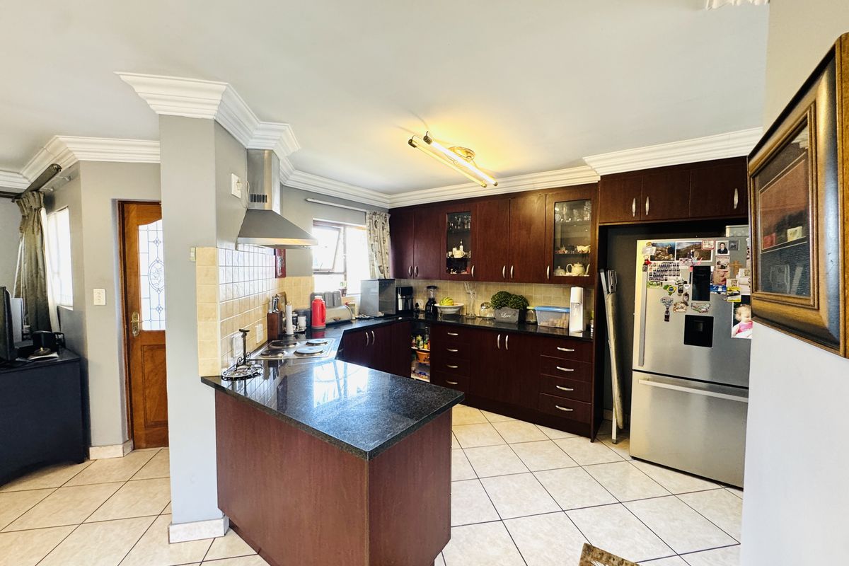 A functional kitchen featuring dark wood cabinetry, granite countertops, a stainless steel extractor fan, and tiled flooring with decorative crown molding.