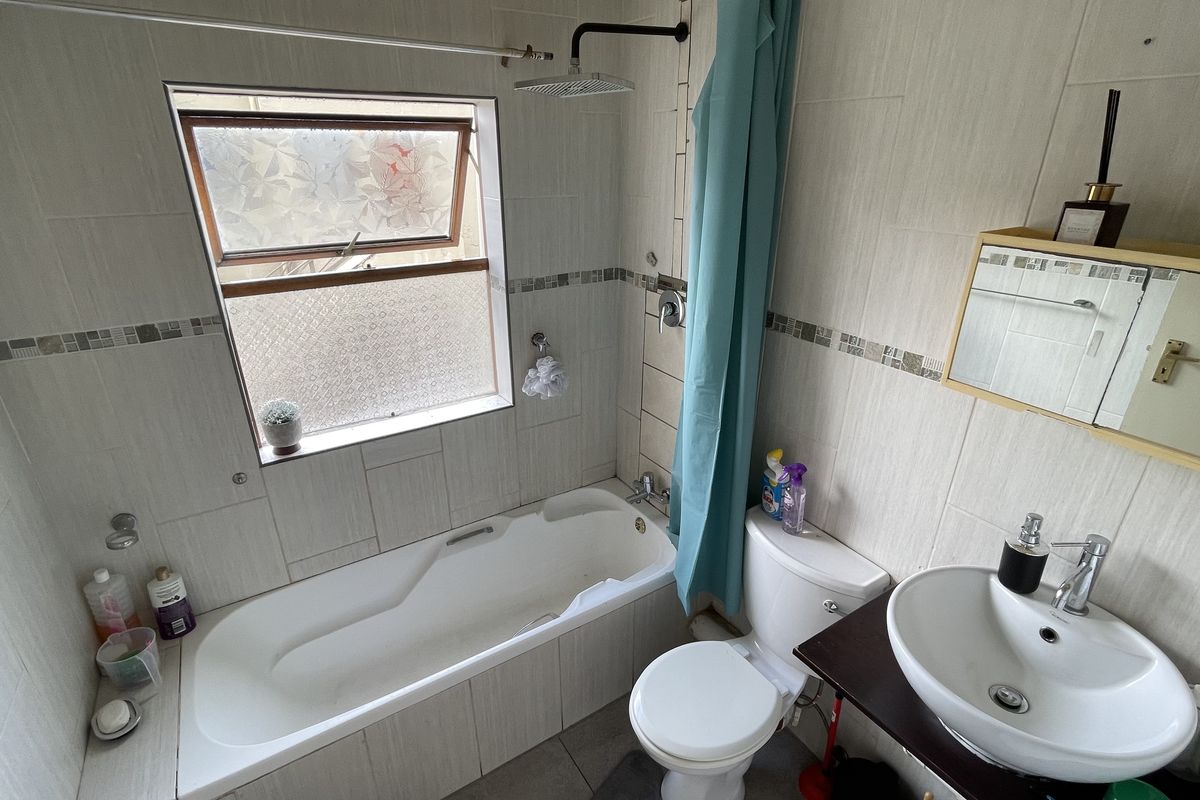 A functional bathroom featuring a bathtub with an overhead shower, a standard toilet, and a wall-mounted washbasin with a medicine cabinet.