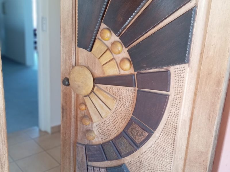 A close-up view of a unique, custom-carved wooden door featuring geometric patterns and textured detailing, set within a tiled interior space.