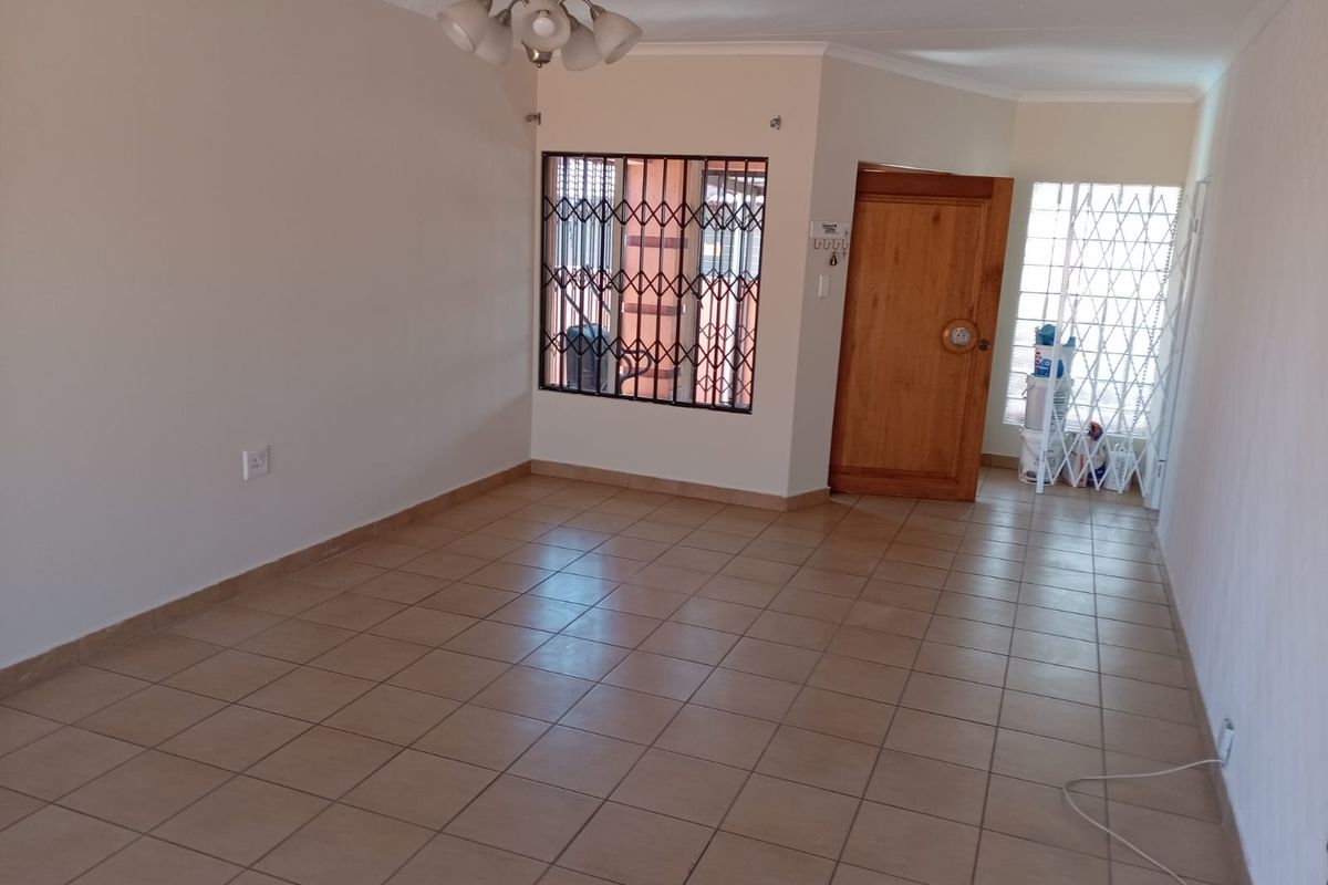 An empty living room featuring neutral tiled flooring, a wooden entrance door, and security bars on the windows.