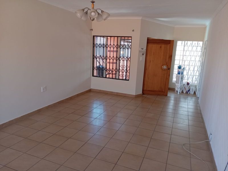 An empty living room featuring neutral tiled flooring, a wooden entrance door, and security bars on the windows.