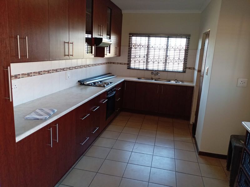 A functional kitchen featuring dark wood cabinetry, laminate countertops, built-in oven and hob, tiled flooring, and a window with security bars.