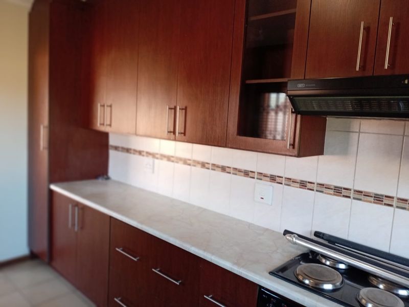 A functional kitchen featuring dark wood-finish cabinetry, a light-toned laminate countertop, tiled backsplash, and a built-in electric hob with an extractor fan.