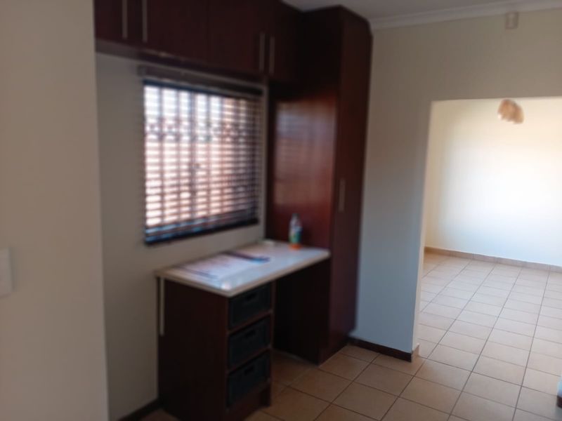 A functional scullery or utility area featuring built-in dark wood cabinetry, tiled flooring, and a window with fitted blinds.