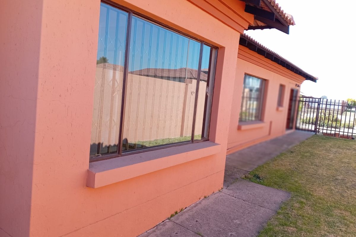 A view of the rear exterior of the house featuring a concrete pathway, tiled roof, and security bars on the windows.