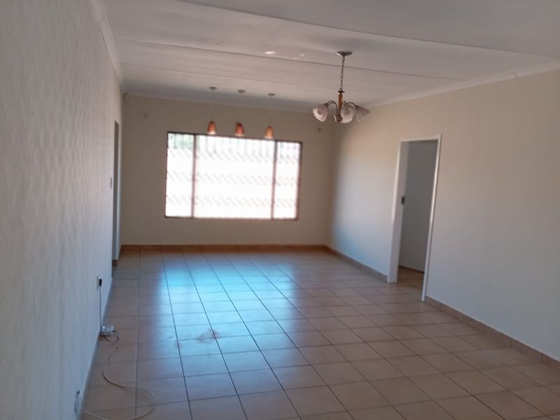 A spacious, empty living area featuring neutral walls, tiled flooring, and multiple ceiling light fixtures, providing a blank canvas for interior design.