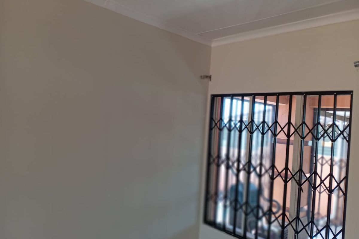 An empty bedroom featuring neutral walls, a ceiling cornice, and a window fitted with a black metal security gate.