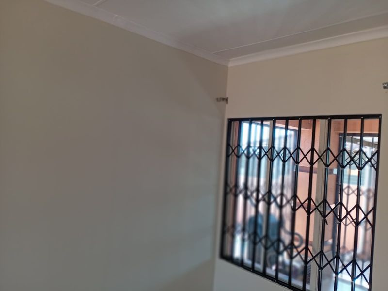 An empty bedroom featuring neutral walls, a ceiling cornice, and a window fitted with a black metal security gate.