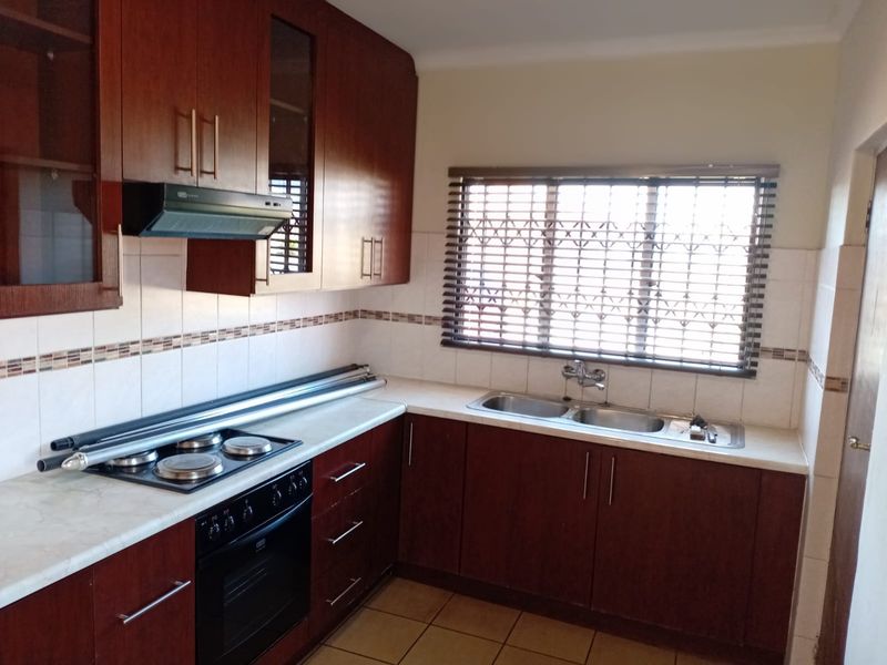 A functional kitchen featuring dark wood cabinetry, laminate countertops, a double basin sink, and built-in cooking appliances with tiled finishes.