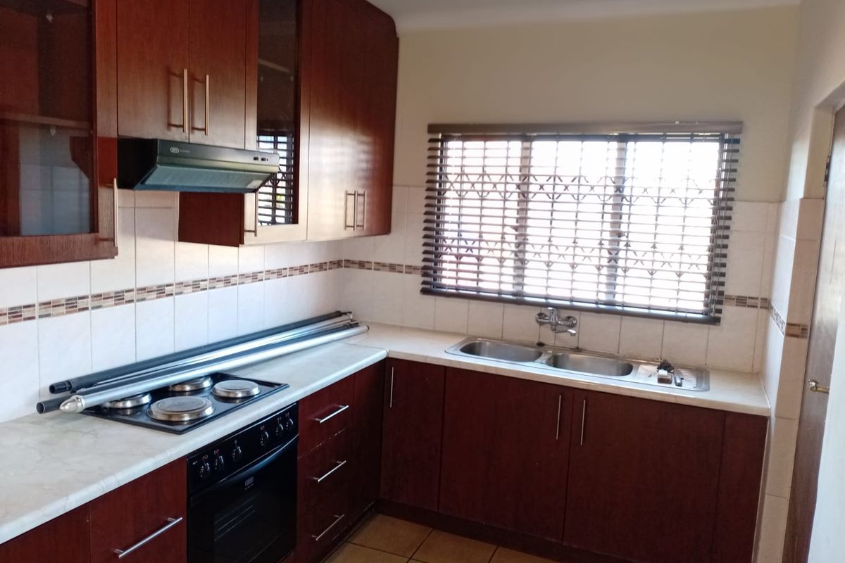 A functional kitchen featuring dark wood cabinetry, laminate countertops, a double basin sink, and built-in cooking appliances with tiled finishes.