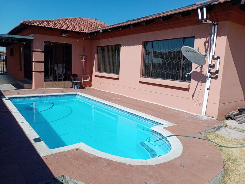 Rear exterior view featuring a swimming pool with tiled surround, set against the house facade with security bars and tiled roofing.