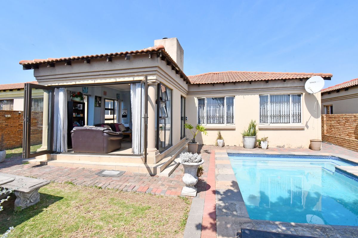 Rear view of the property featuring a swimming pool, paved patio area, and access to the living space through large glass doors.