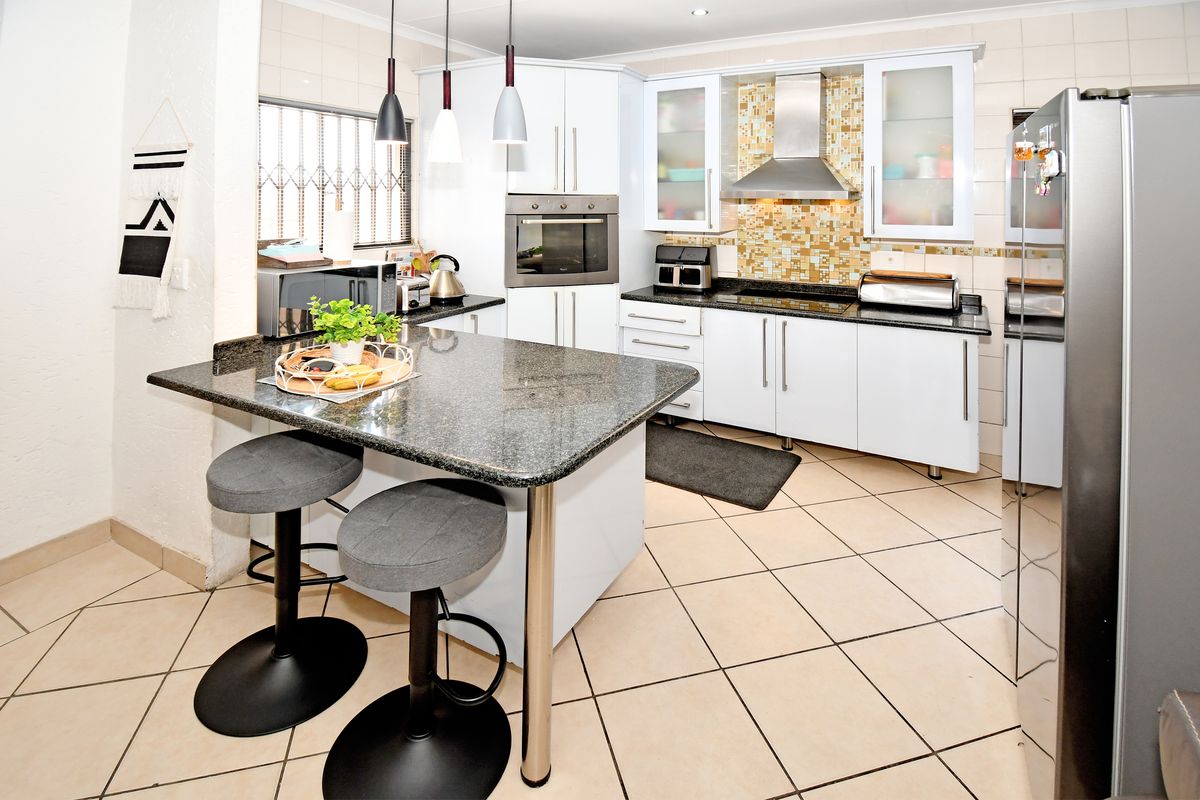 Modern kitchen featuring granite countertops, a central island, built-in oven, extractor fan, and stylish mosaic tile backsplash with ample storage cabinetry.
