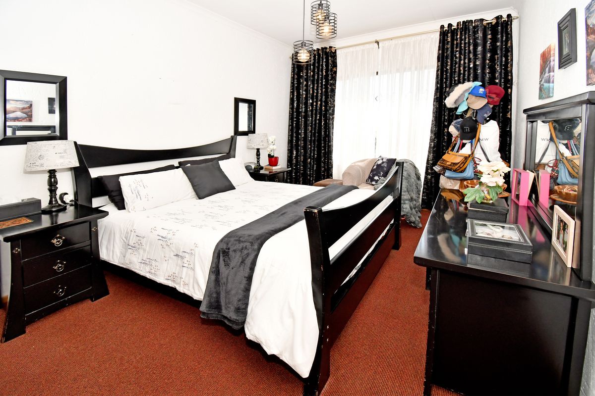 A bedroom featuring carpeted flooring, pendant lighting, and large windows with curtain tracks, offering a functional space for rest.