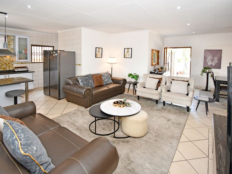 Spacious open-plan living area featuring a modern kitchen with granite countertops, mosaic backsplash, and tiled flooring throughout, leading to an outdoor entrance.