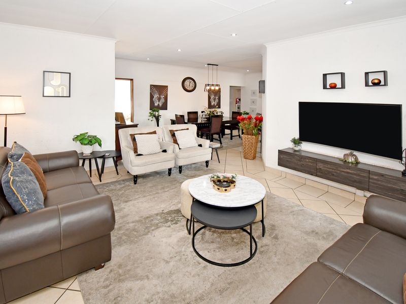 Spacious open-plan living and dining area featuring neutral tiled flooring, recessed downlighting, and a modern floating media console.