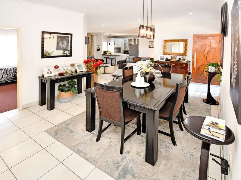 Spacious open-plan living and dining area featuring tiled flooring, modern pendant lighting, and a solid wood entrance door, flowing into the kitchen.