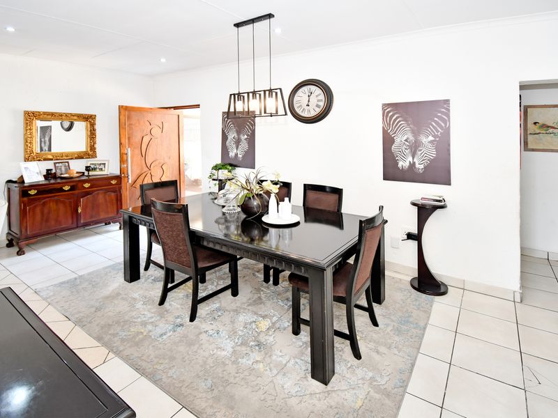 A well-lit dining room featuring tiled flooring, a modern pendant light fixture, and a solid wood entrance door.