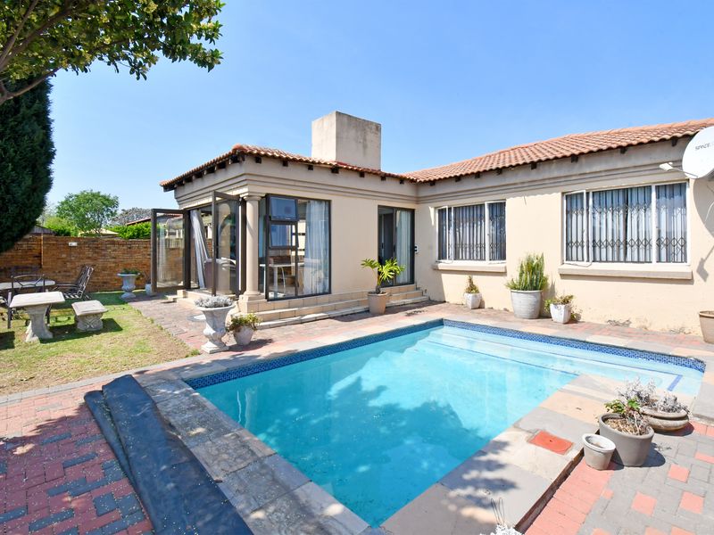 Rear exterior view featuring a swimming pool, paved patio area, and direct access to the home with security-fitted windows and a chimney.