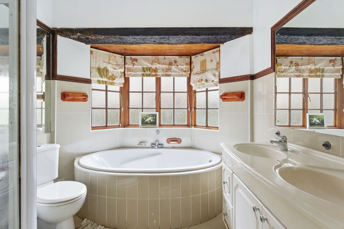 A bathroom featuring a corner bathtub, double vanity, and a bay window with exposed timber beam detailing.