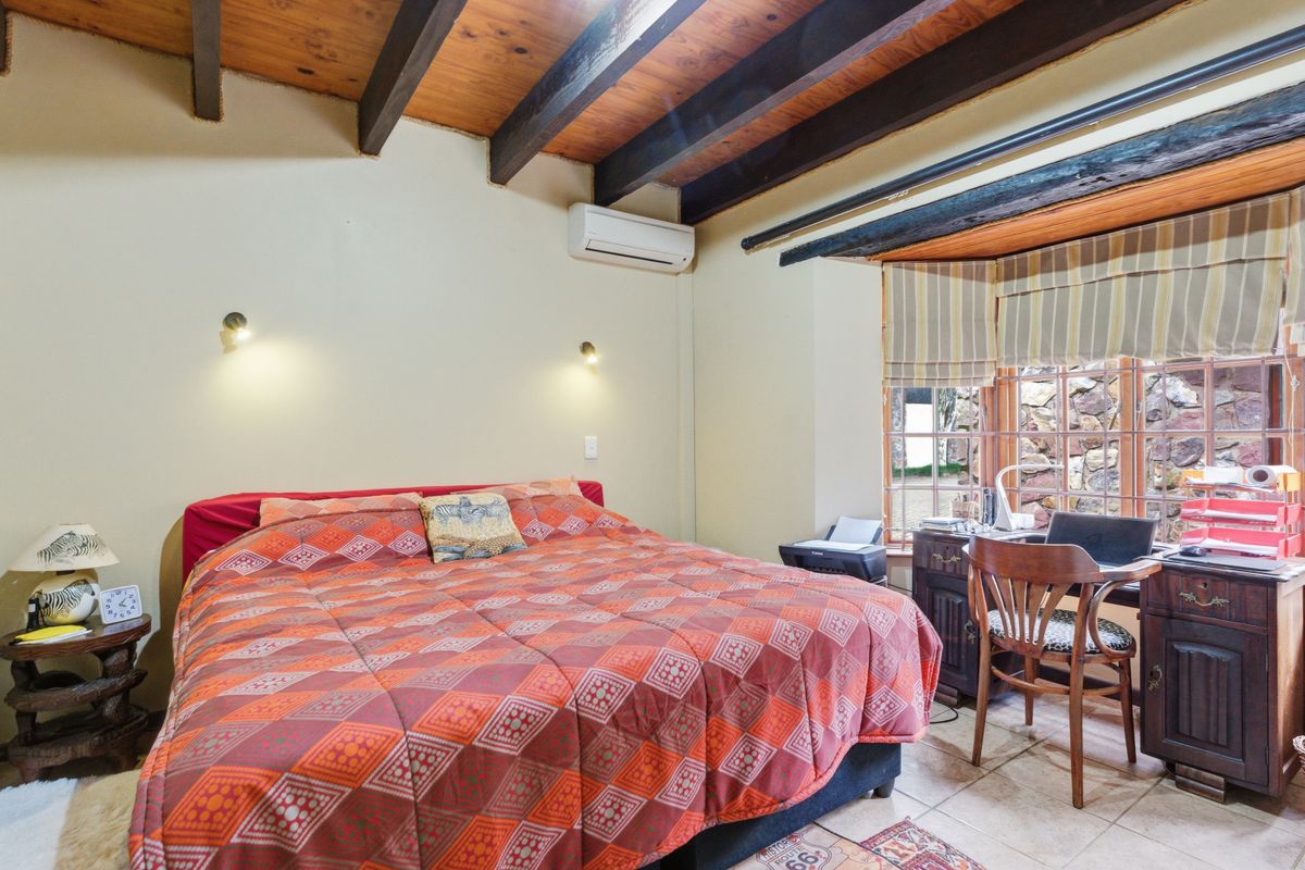 A bedroom featuring exposed timber ceiling beams, tiled flooring, and a bay window with natural light, equipped with a wall-mounted air conditioning unit.