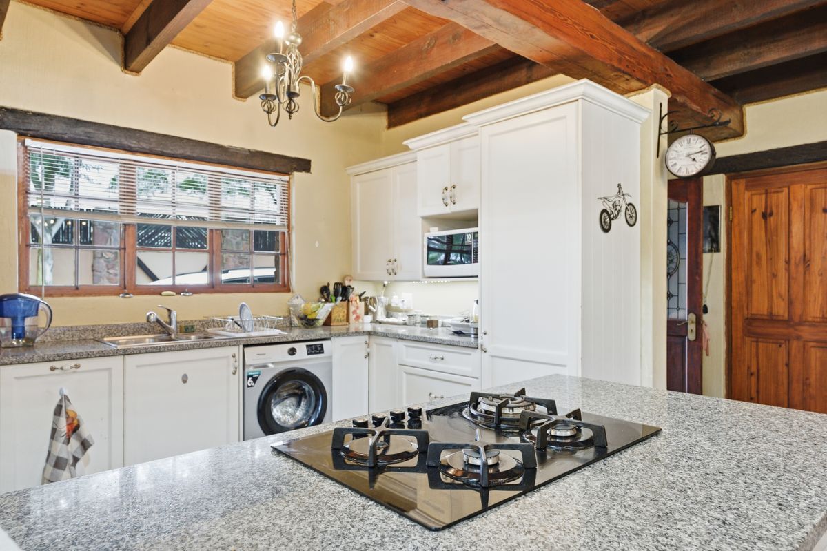 A well-appointed kitchen featuring granite countertops, a built-in gas hob, white cabinetry, and rustic exposed timber ceiling beams.