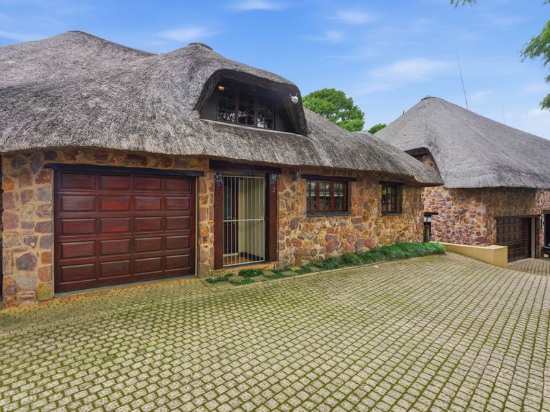 Front elevation of a townhouse featuring traditional thatched roofing, stone facade, paved driveway, and integrated garage access.