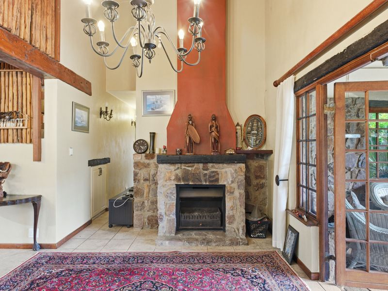 A rustic living room featuring a prominent stone fireplace, exposed timber beams, and direct access to the outdoor area through timber-framed glass doors.