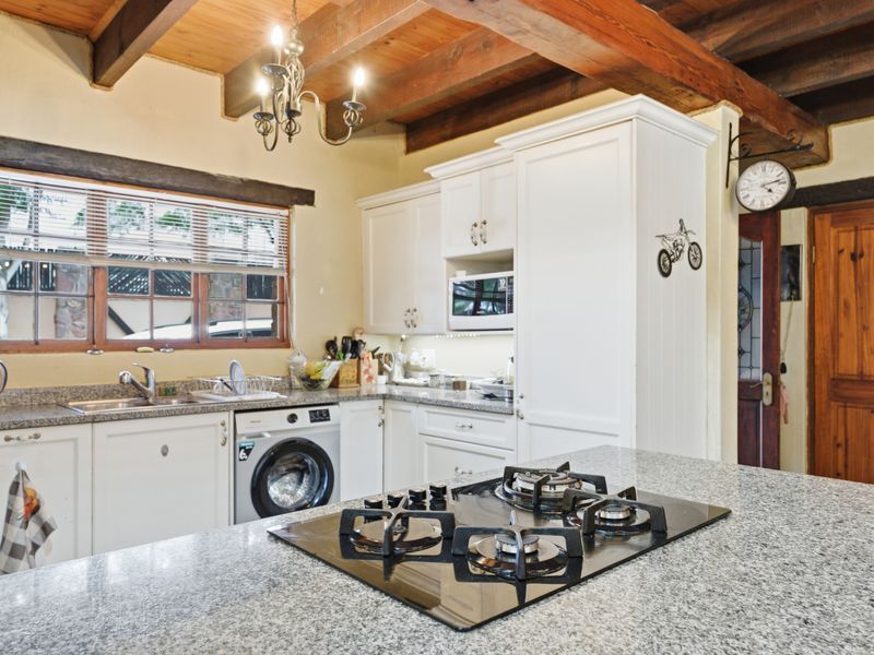 A well-appointed kitchen featuring granite countertops, a built-in gas hob, white cabinetry, and rustic exposed timber ceiling beams.