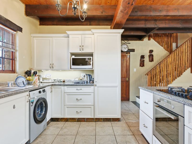 A well-appointed kitchen featuring white cabinetry, granite countertops, built-in appliances, and rustic exposed timber ceiling beams, adjacent to a wooden staircase.