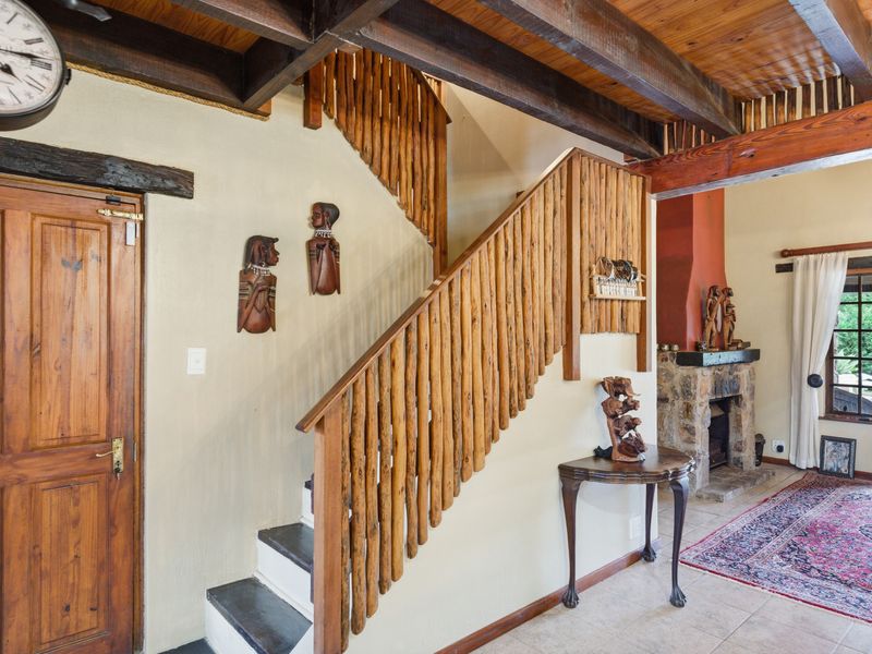 Living area featuring exposed timber ceiling beams, a rustic timber staircase, and a stone fireplace, creating a warm and traditional atmosphere.