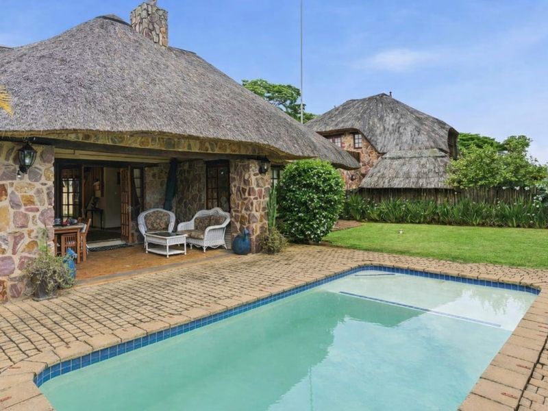 Outdoor pool area featuring a swimming pool, brick paving, and a covered patio with traditional thatched roofing and stone wall finishes.
