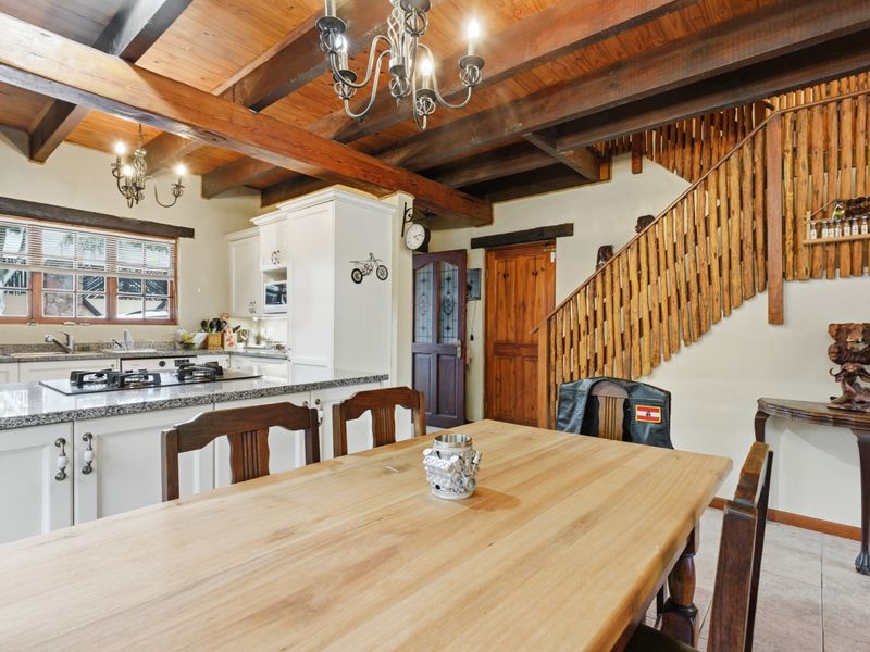 Open-plan kitchen and dining area featuring exposed timber ceiling beams, granite countertops, a built-in gas hob, and a rustic timber staircase.