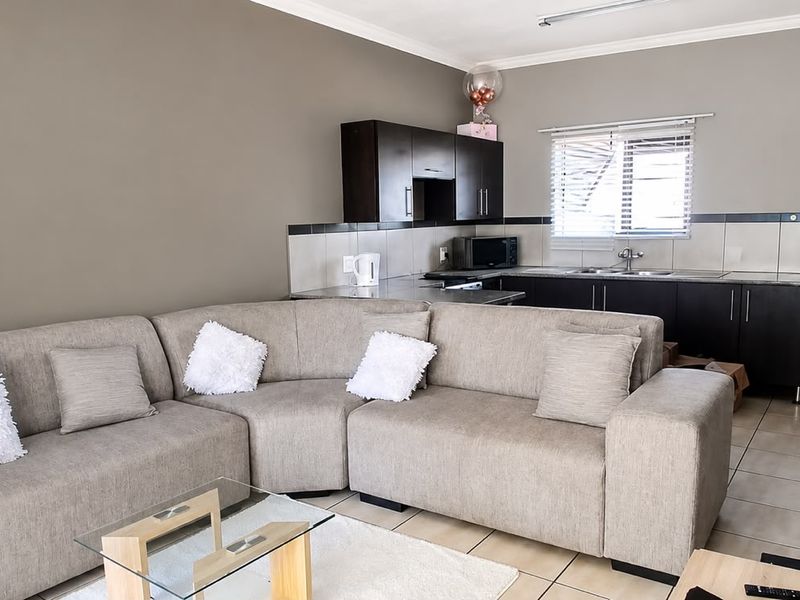 Open-plan living area featuring a compact kitchen with dark cabinetry, tiled backsplash, and neutral wall tones, seamlessly connected to the lounge space.