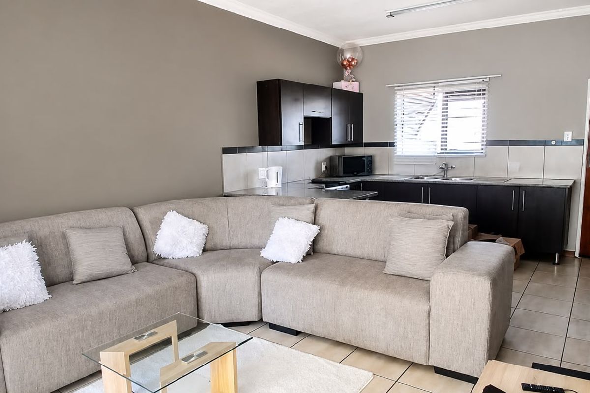 Open-plan living area featuring a compact kitchen with dark cabinetry, tiled backsplash, and neutral wall tones, seamlessly connected to the lounge space.