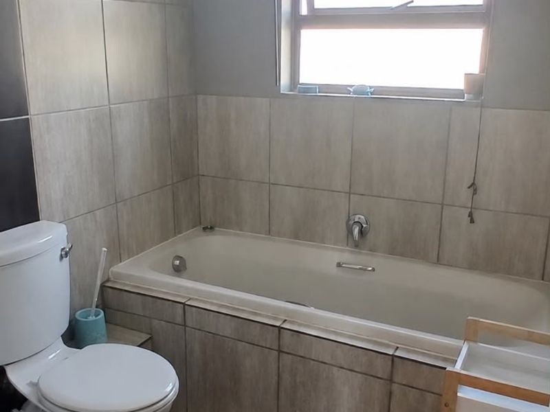 A functional bathroom featuring a built-in bathtub, toilet, and neutral wall and floor tiling with natural light from a window.