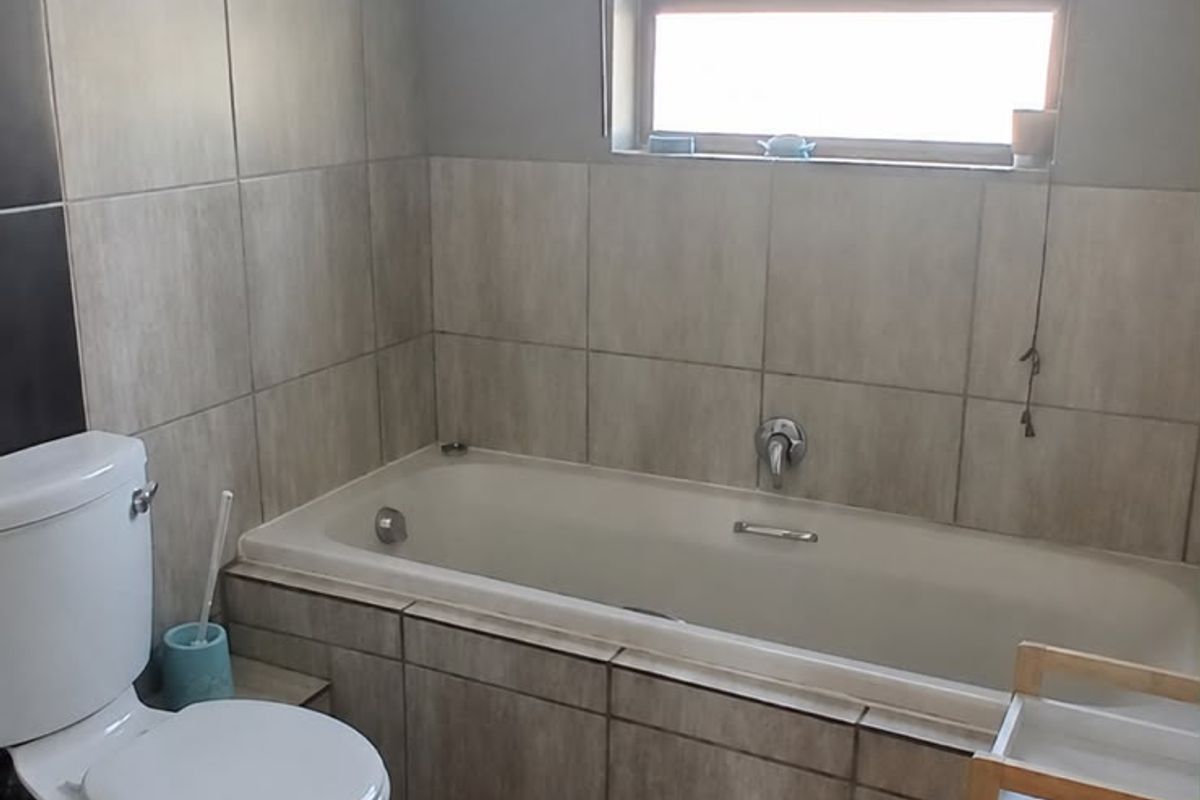 A functional bathroom featuring a built-in bathtub, toilet, and neutral wall and floor tiling with natural light from a window.