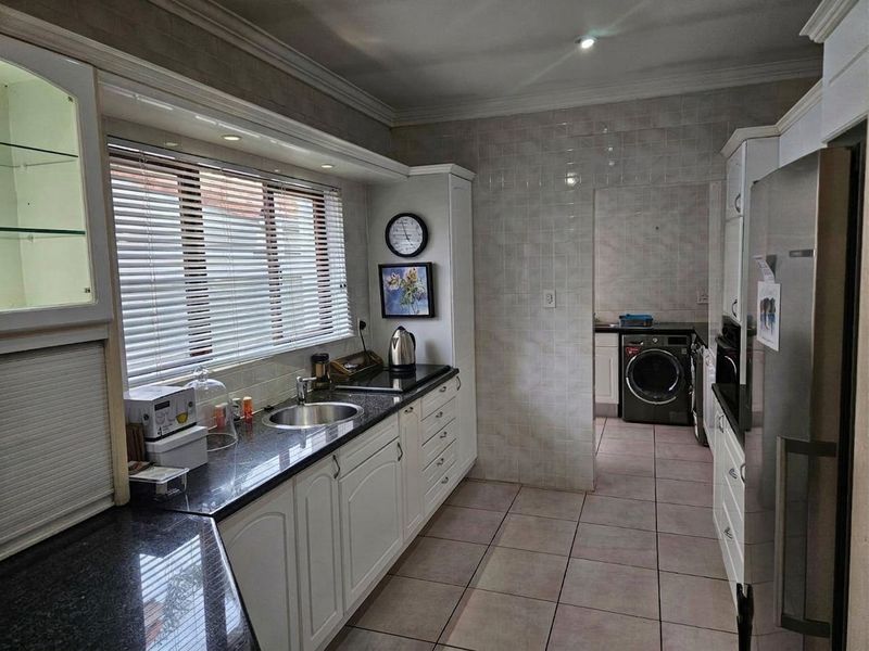 A functional kitchen featuring granite countertops, white cabinetry, tiled backsplash, and an adjoining laundry area with tiled flooring throughout.