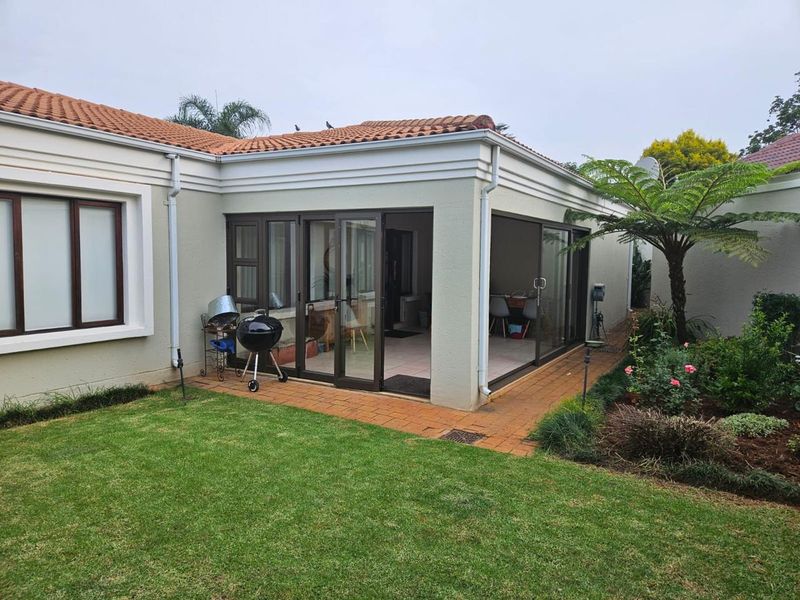 Rear view of the house featuring a paved patio area, sliding glass doors, and a well-maintained garden with terracotta roof tiles.