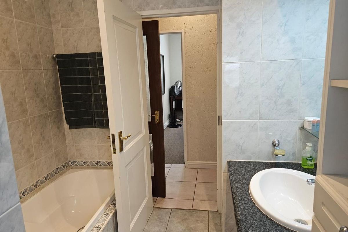 A functional bathroom featuring a built-in bathtub, vanity basin with granite countertop, and neutral ceramic wall and floor tiling.
