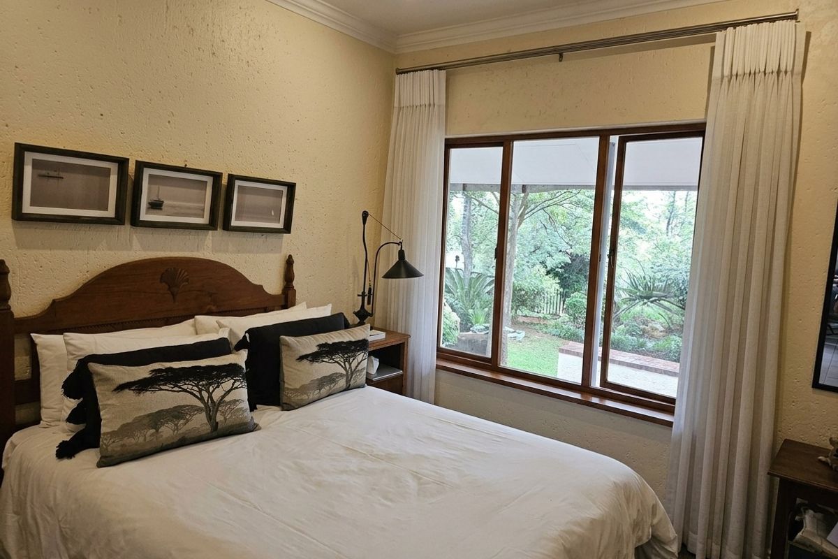A cozy bedroom featuring textured walls, wooden window frames, and direct access to garden views through large windows.