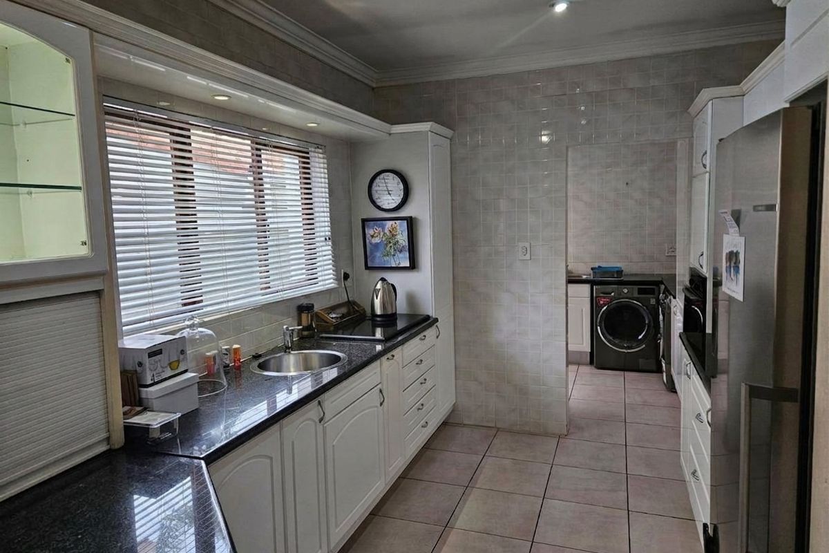 A functional kitchen featuring granite countertops, white cabinetry, tiled backsplash, and an adjoining laundry area with tiled flooring throughout.