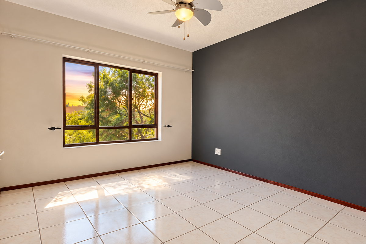 A bright, empty bedroom featuring tiled flooring, a ceiling fan, and a contrasting dark accent wall with a large window.