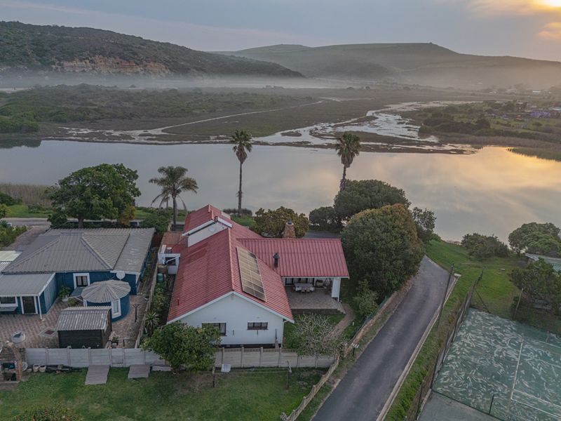Aerial view of a residential property featuring a metal roof with solar panels, a private tennis court, and scenic views of the adjacent river.