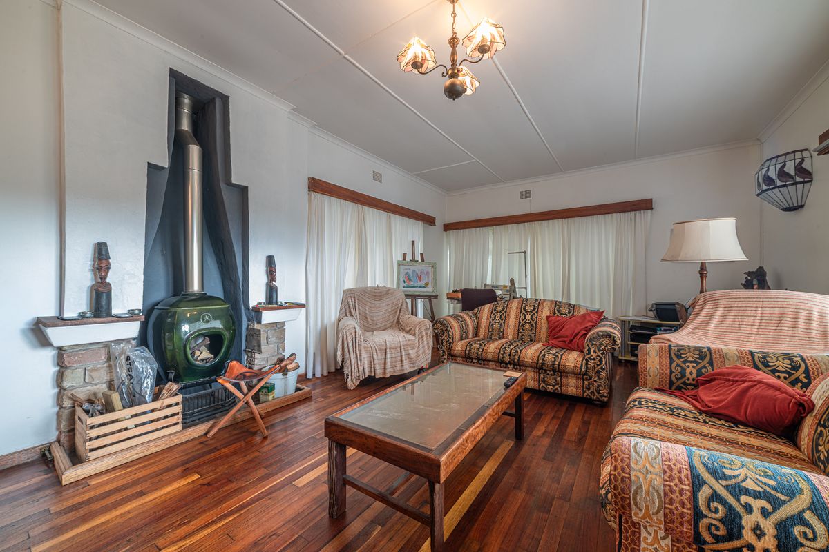 A living room featuring polished hardwood flooring and a prominent green freestanding fireplace with a stone hearth.