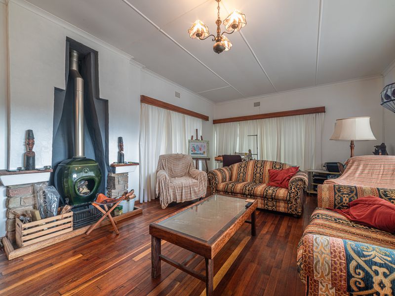A living room featuring polished hardwood flooring and a prominent green freestanding fireplace with a stone hearth.